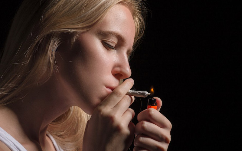 Жінка закурює сигарету з марихуаною фото